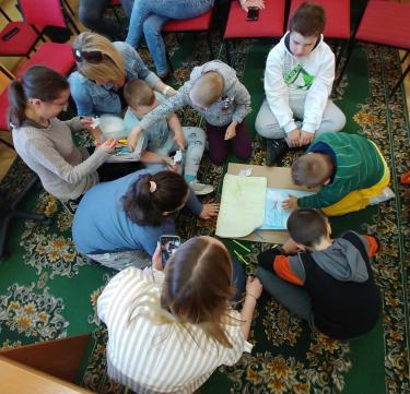 Grupka uczniów wraz z nauczycielką siedzą pochyleni nad obrazkami i kartką - zajęcia o Calineczce