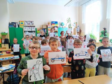 Uczniowie SP 1 w Przemyślu, stoją w ławeczkach szkolnych i prezentują rysunki wykonane podczas zajęć o odwadze.